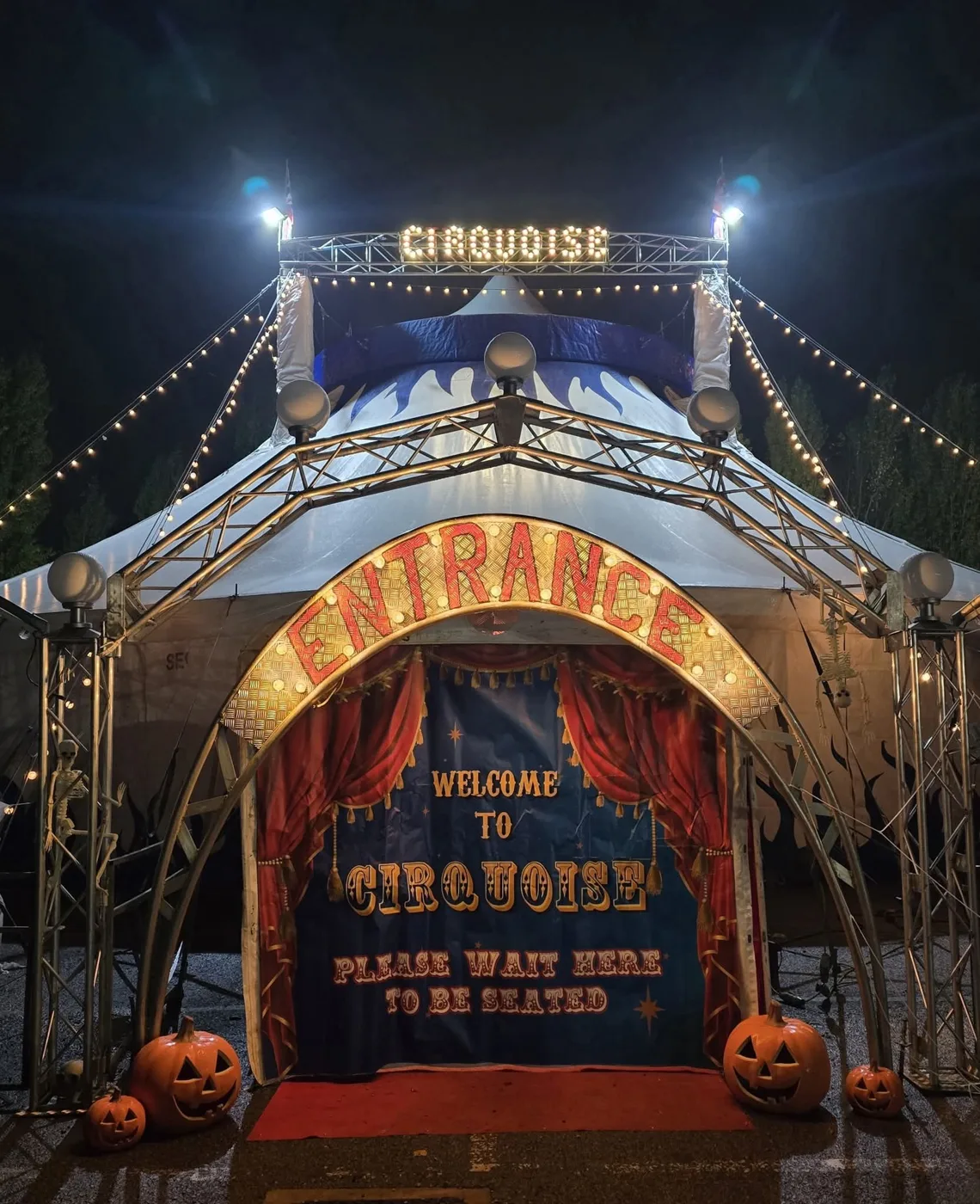 The entrance to the Cirquoise big top, lit up at night and dressed with pumpkins and skeletons